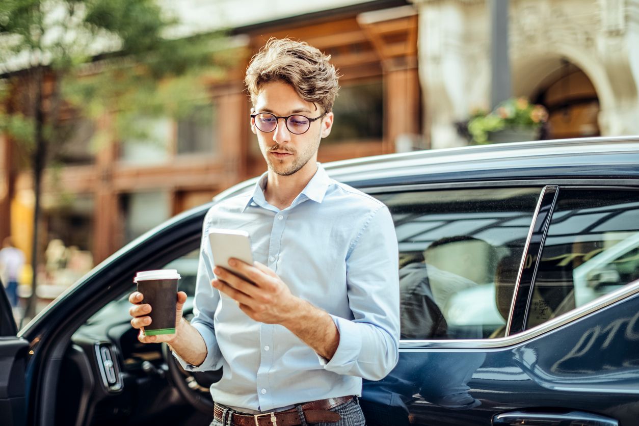 Ein Mann steht neben einem Auto, prüft die Preise für Wallboxen auf seinem Mobiltelefon 