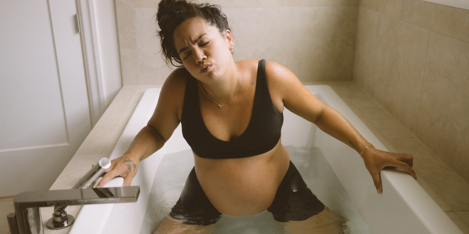Pregnant mother, who completed the Momday pregnancy workout program, squatting in bathtub preparing for labor.