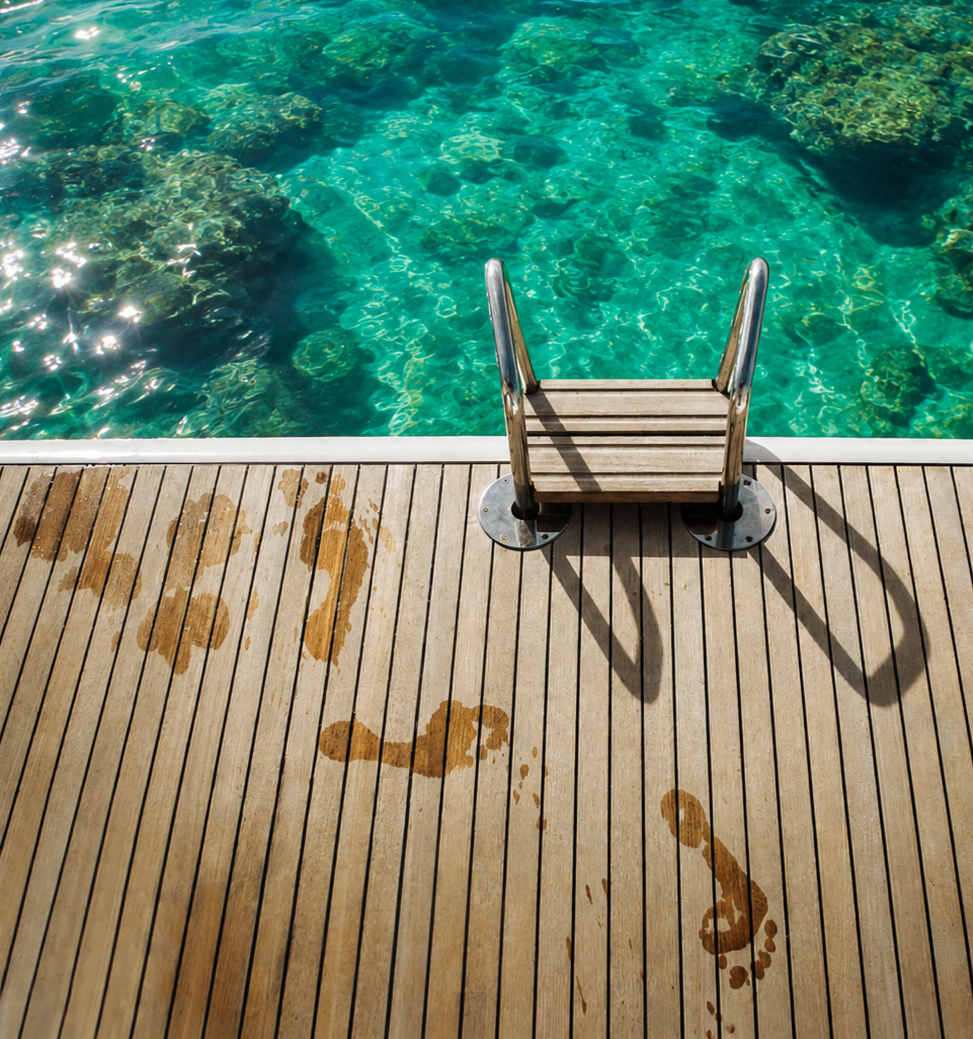 A rolled Atollier towel and a glass of sparkling water with lime on a jetty beside a swim ladder, over turquoise reef at golden hour