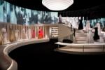 View of the final gallery, The Revived Allure, with many Chanel pieces on display around the room and up a sweeping staircase, there are projections from archive footage of fashion shows in Chanel's salon, these images are reflected in a mirrored wall facing the screens. The scene references Chanel's salon in Paris. From Gabrielle Chanel. Fashion Manifesto at the V&A Museum London. Soundscape by Coda to Coda.