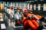 Models of race car drivers lined up in two rows on a raised platform in the middle of a large gallery. At Formula 1 Exhibition. Soundscape by Coda to Coda