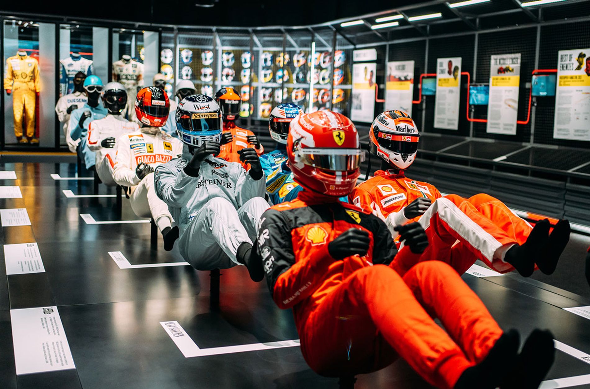 Models of race car drivers lined up in two rows on a raised platform in the middle of a large gallery. At Formula 1 Exhibition. Soundscape by Coda to Coda