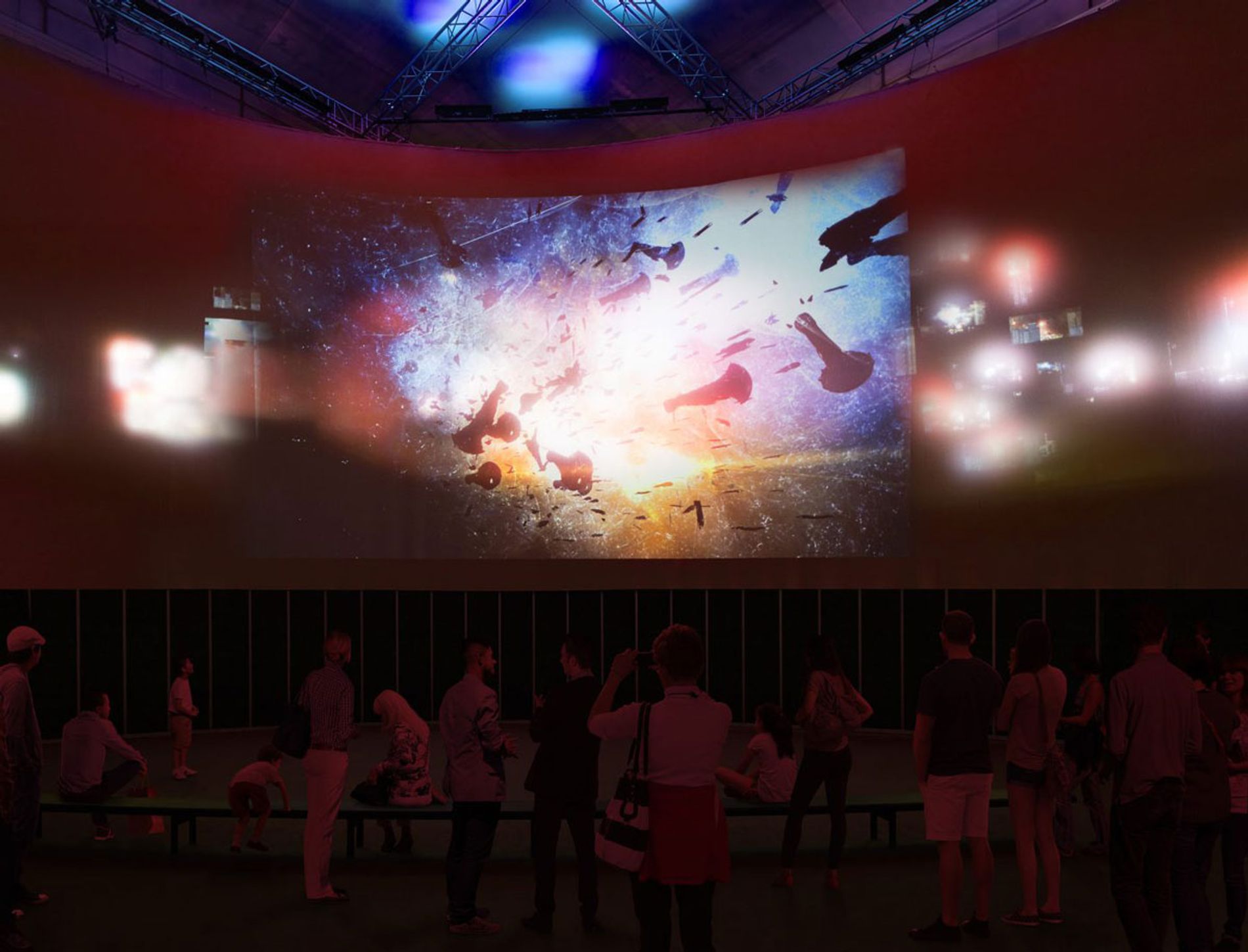 Image shows a large LED screen showing a massive explosion of light, an audience watches below. From Videogames: Design/Play/Disrupt at the V&A London. Exhibition soundscape by Coda to Coda