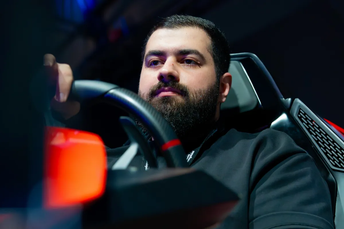 Bearded man in a black top at the wheel of a Lamborghini-styled simulator under stage lighting