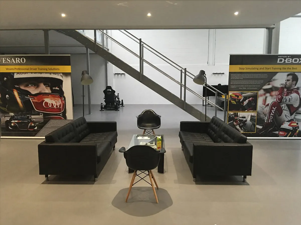 Vesaro showroom lounge with black sofas, a staircase and Vesaro and D-BOX banners on the walls