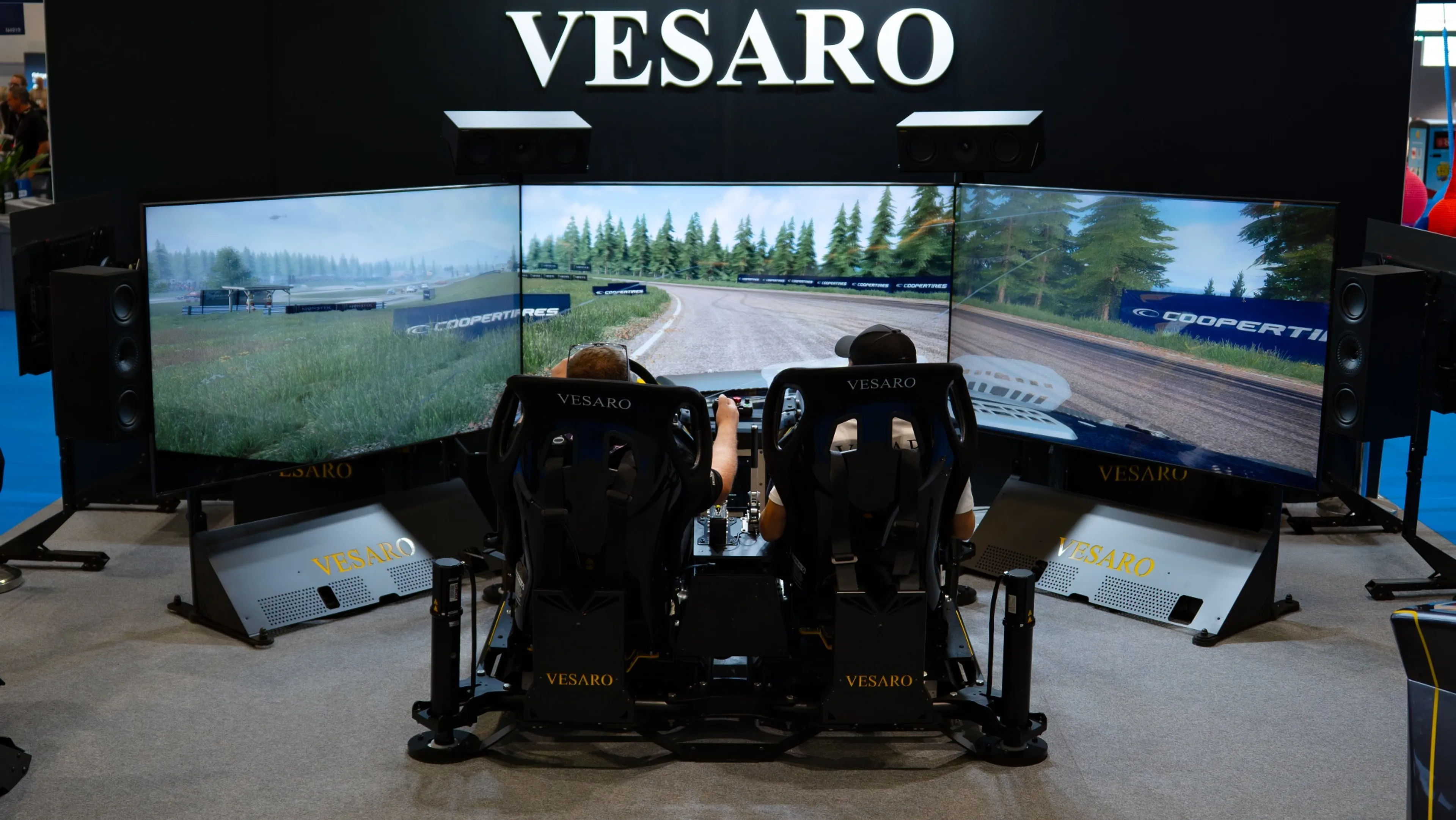 Two people in the two-seat Vesaro Rally simulator in front of its triple screens on the IAAPA stand