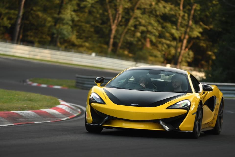 Yellow McLaren sports car with black bonnet cornering on a racetrack kerb