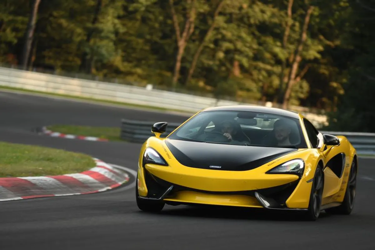 Yellow McLaren sports car with black bonnet cornering on a racetrack kerb