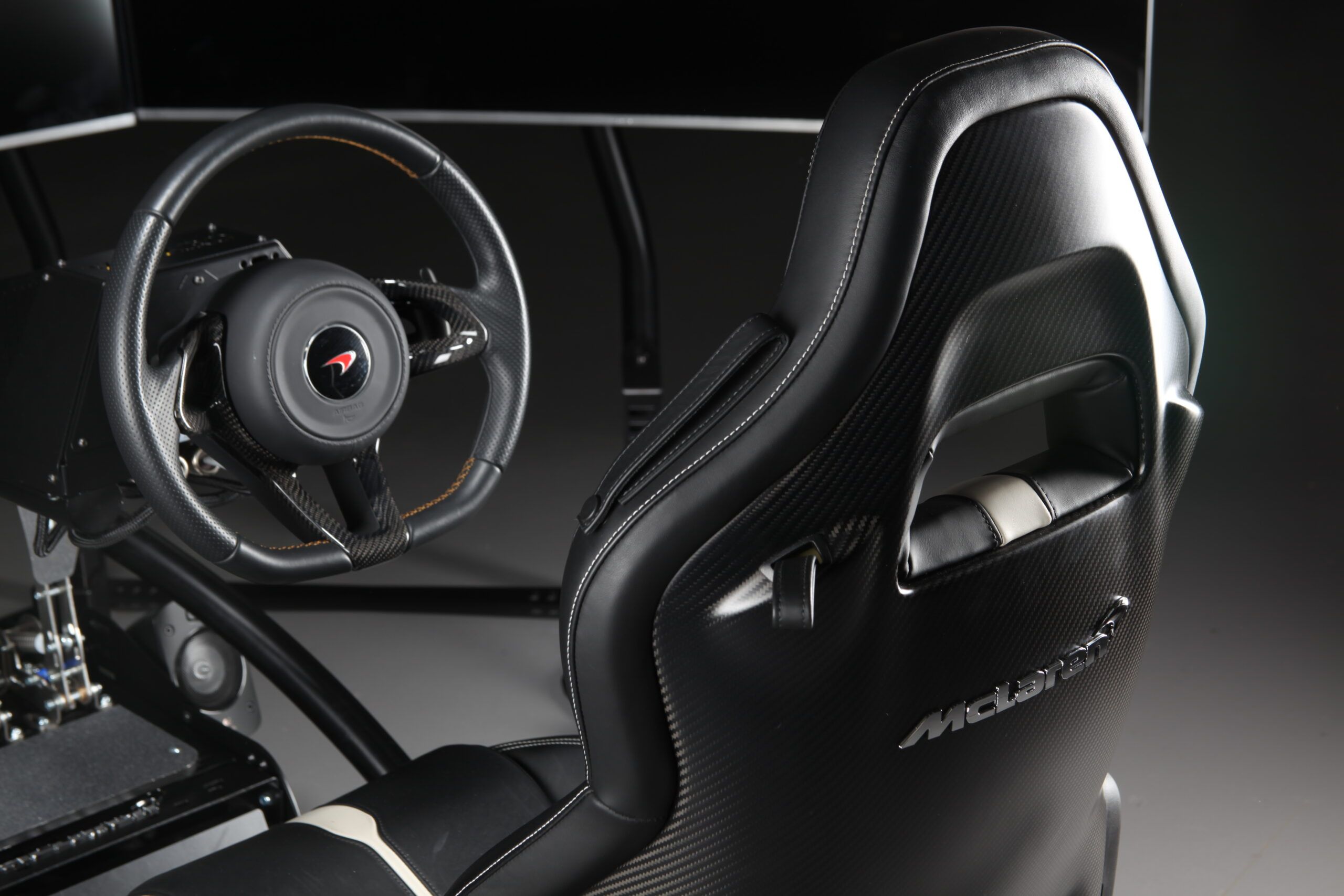 McLaren-branded bucket seat and steering wheel of a Vesaro simulator in low-key studio lighting