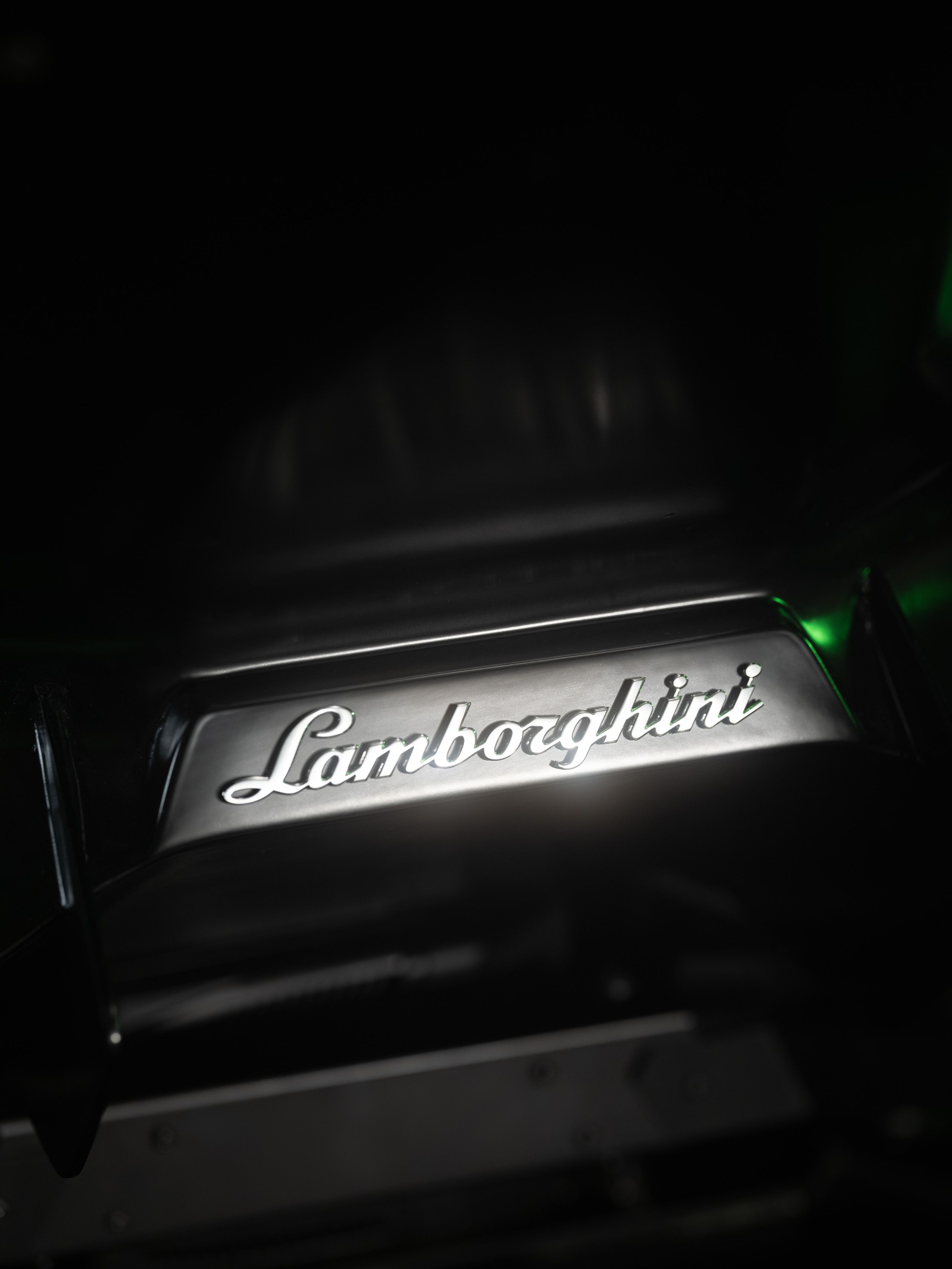 Illuminated Lamborghini script badge glowing in white against a dark background, with a hint of green light