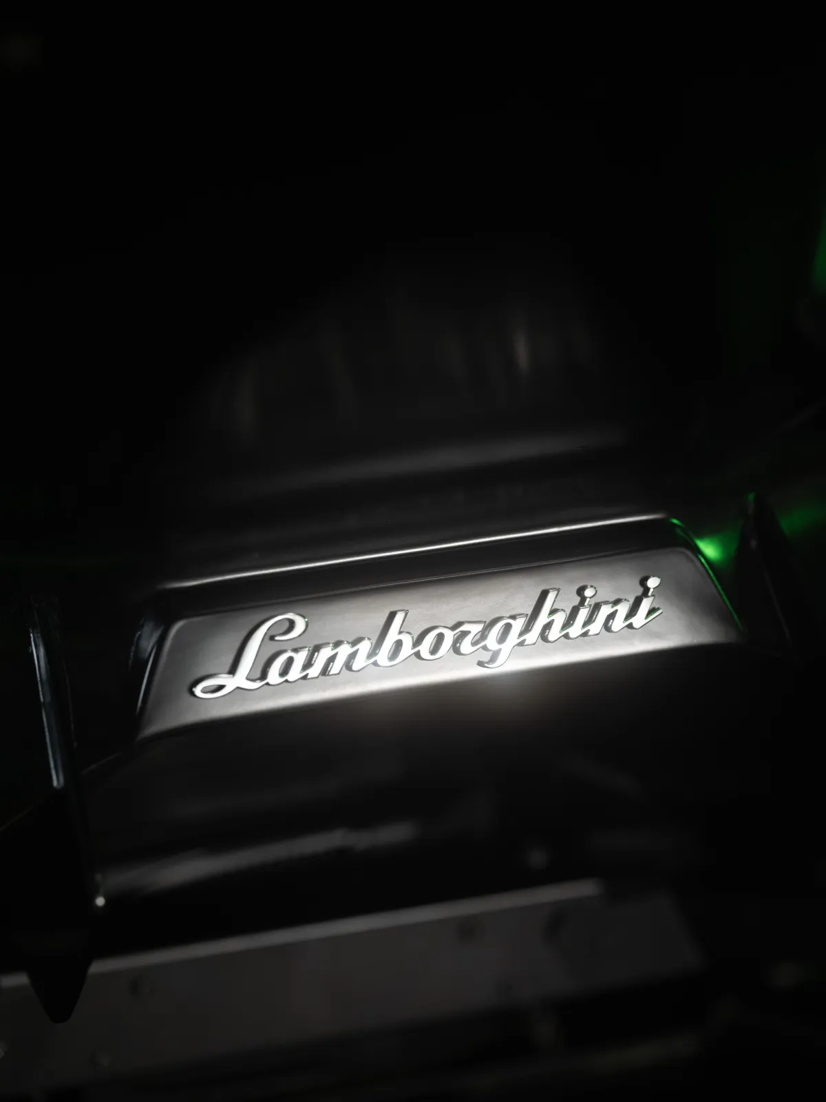 Illuminated Lamborghini script badge glowing in white against a dark background, with a hint of green light
