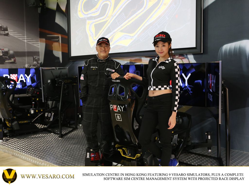 Man and woman in race-style outfits posing beside a Vesaro simulator seat numbered 8 in a sim centre