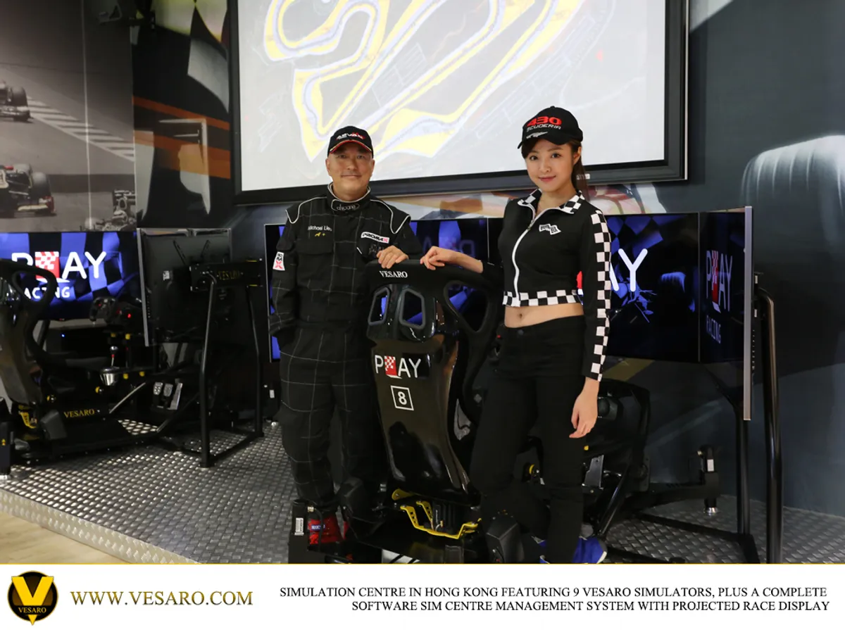 Man and woman in race-style outfits posing beside a Vesaro simulator seat numbered 8 in a sim centre