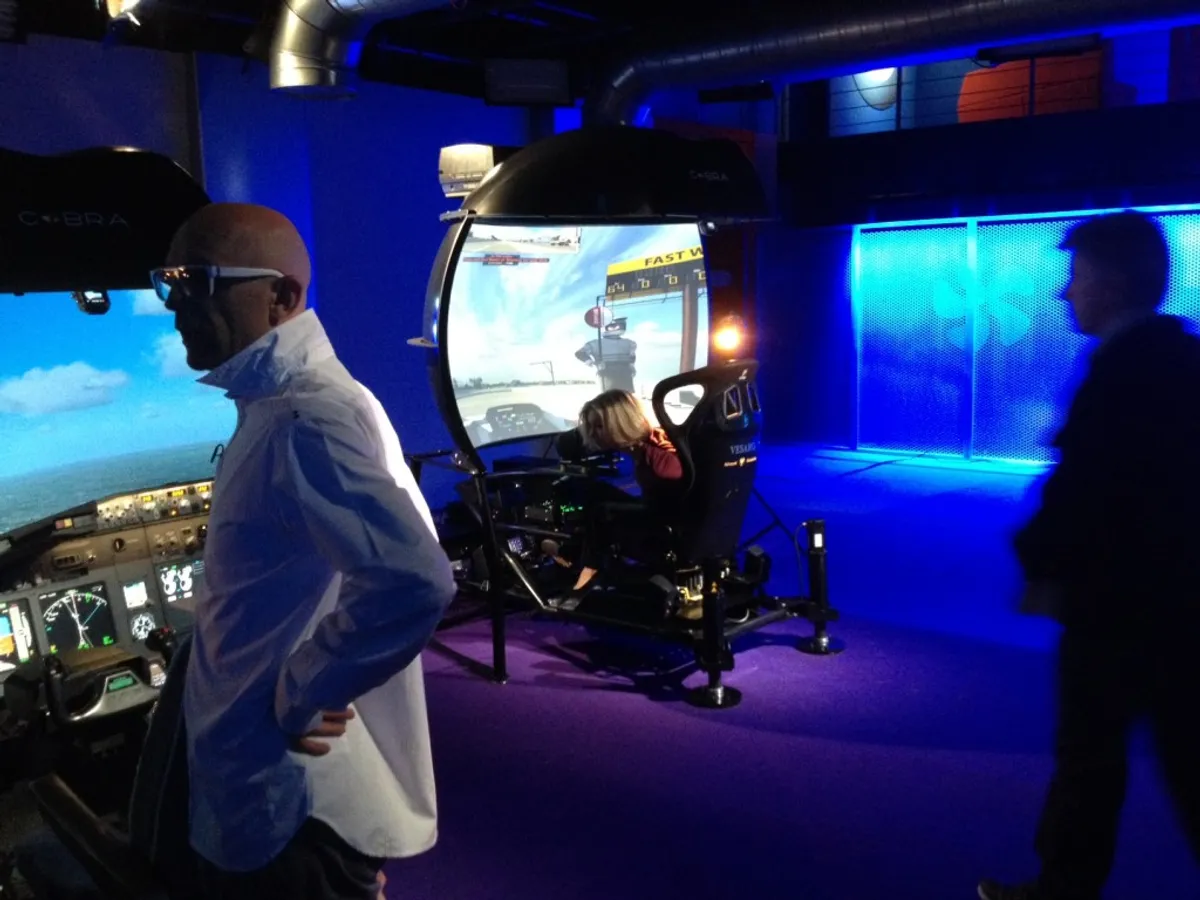 Visitors at a blue-lit exhibition stand with a flight simulator cockpit and a motion simulator with dome screen