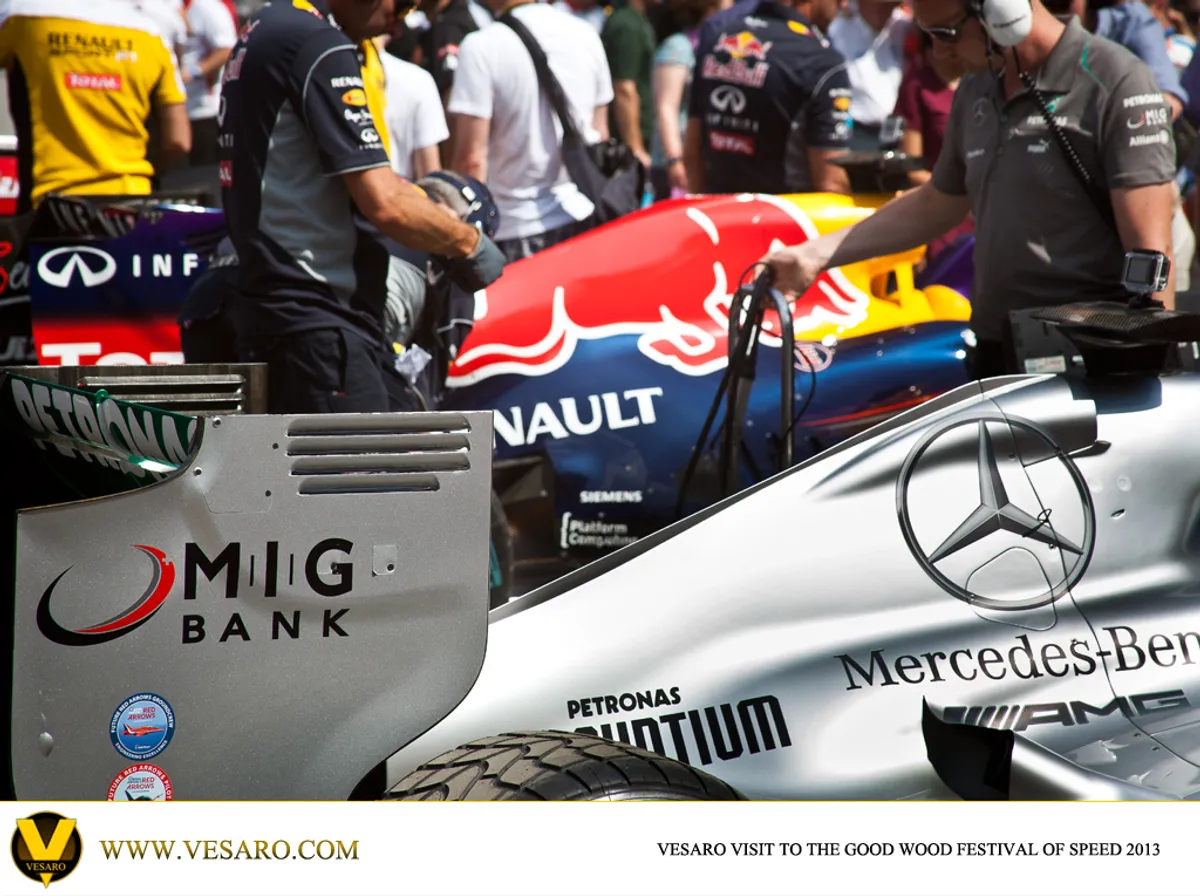 Mechanics at a Red Bull and Mercedes F1 car in the Goodwood paddock, MIG Bank sponsor logos visible