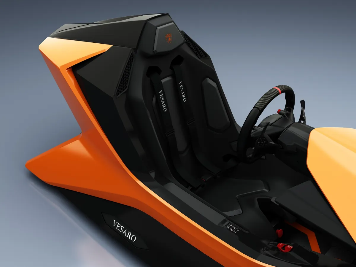 Close view of the orange Prestigio cockpit showing the black bucket seat, harness, steering wheel and Vesaro badge