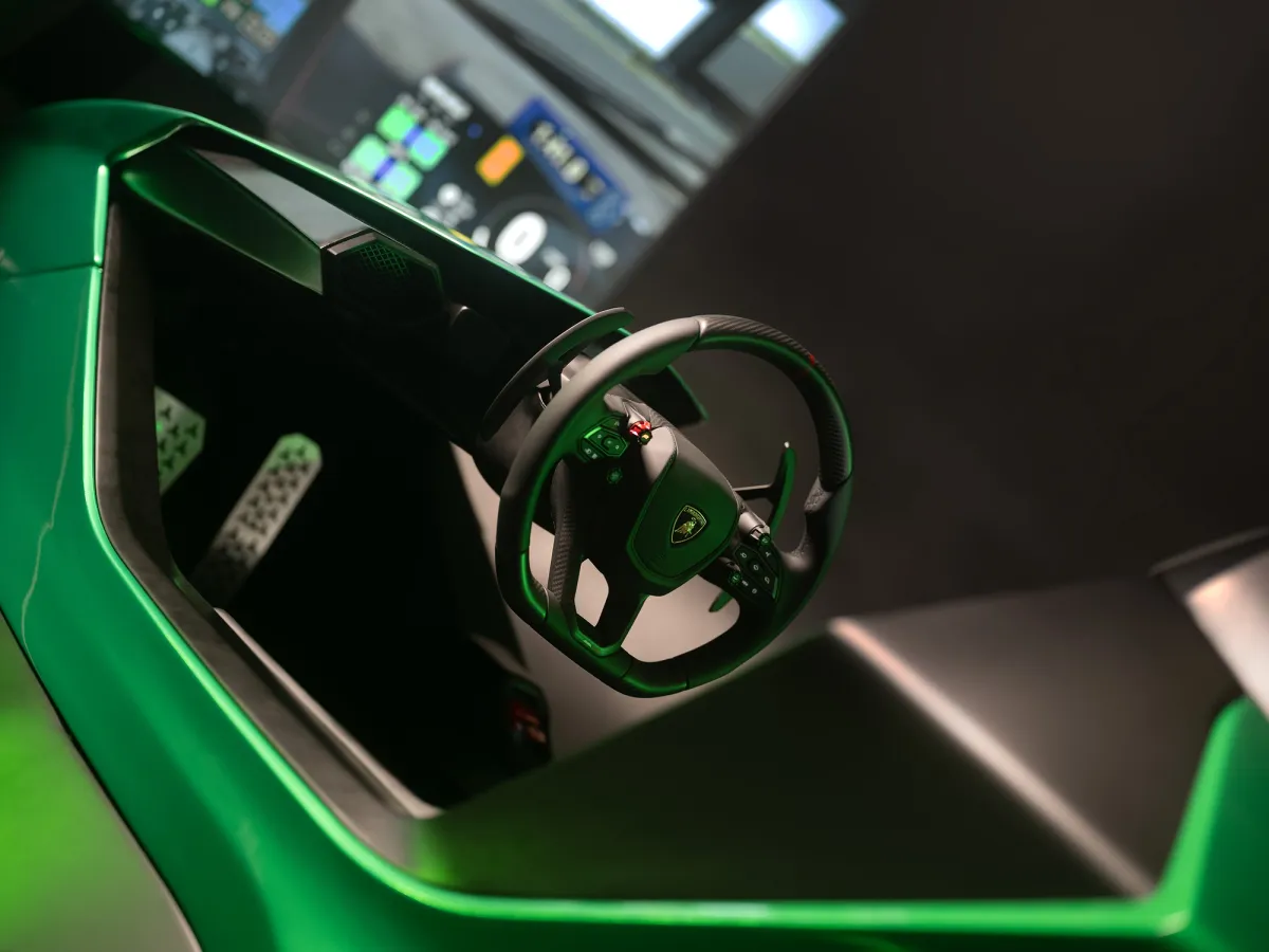 Green-lit Lamborghini simulator cockpit with steering wheel and pedals in front of a large screen