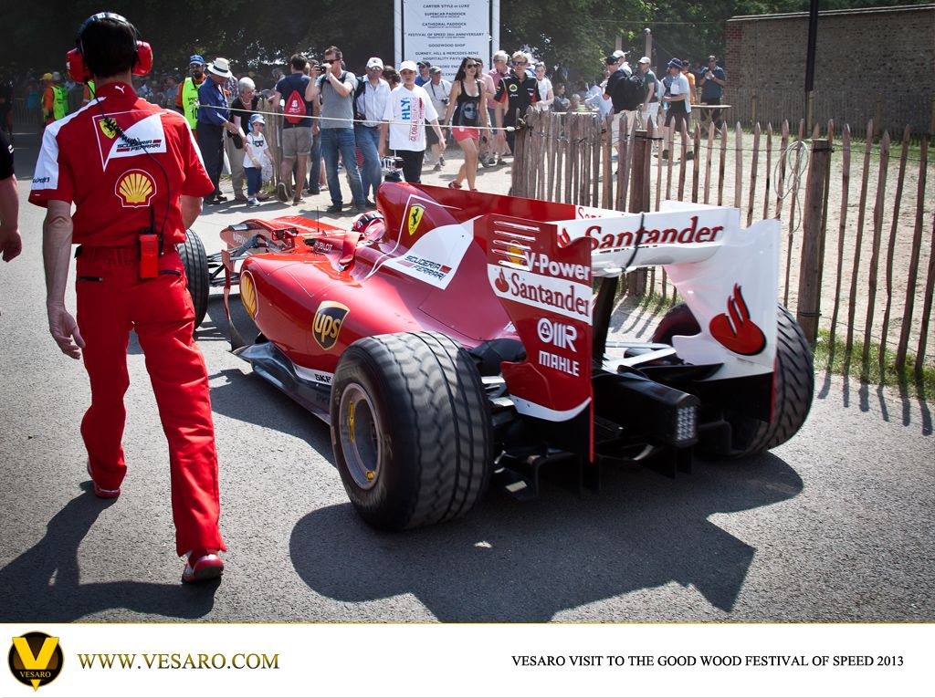 Red Ferrari F1 car with Santander livery seen from the rear, with a mechanic in red overalls at Goodwood