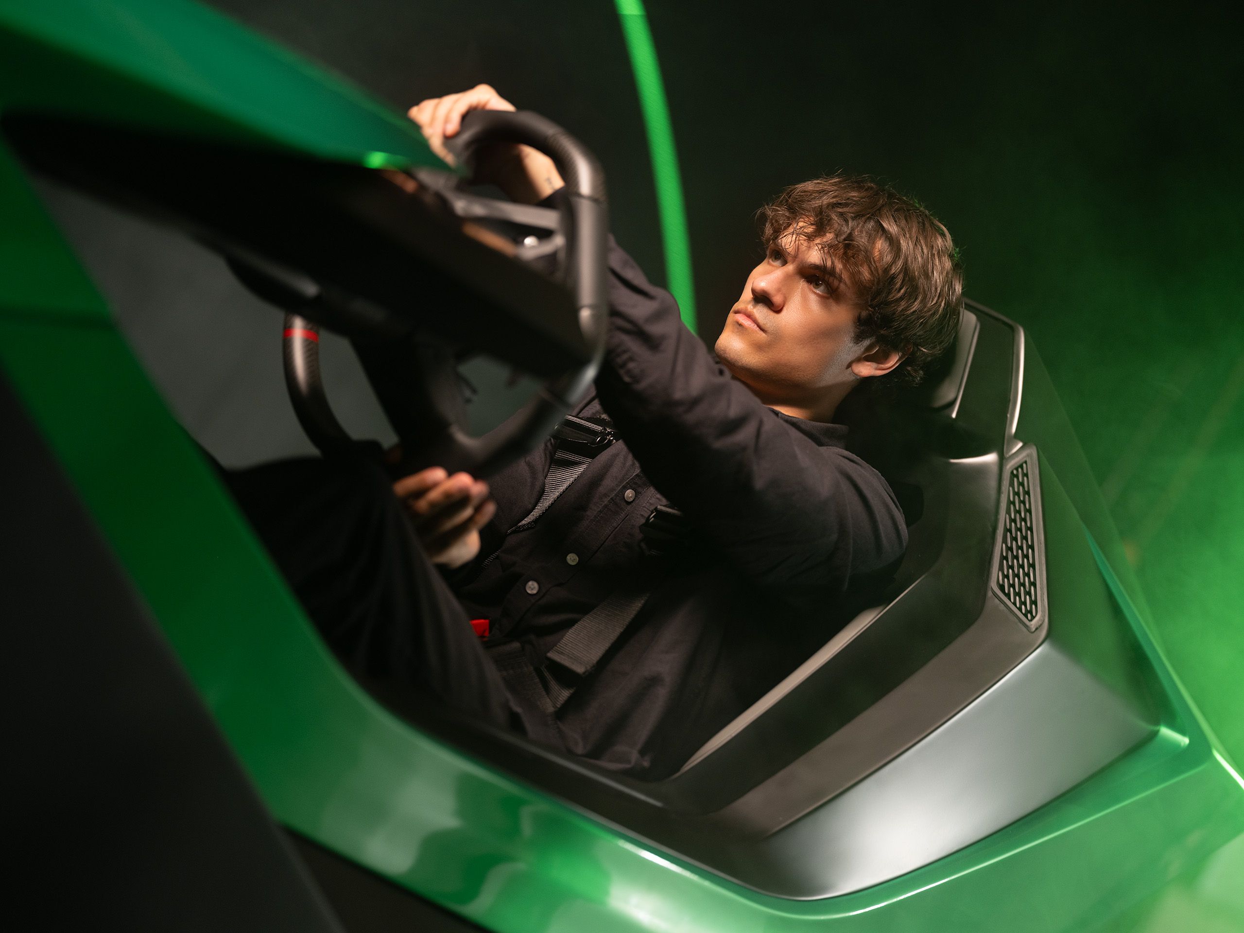 Young man gripping the steering wheel in a green Lamborghini-themed Vesaro racing simulator cockpit, lit with green light