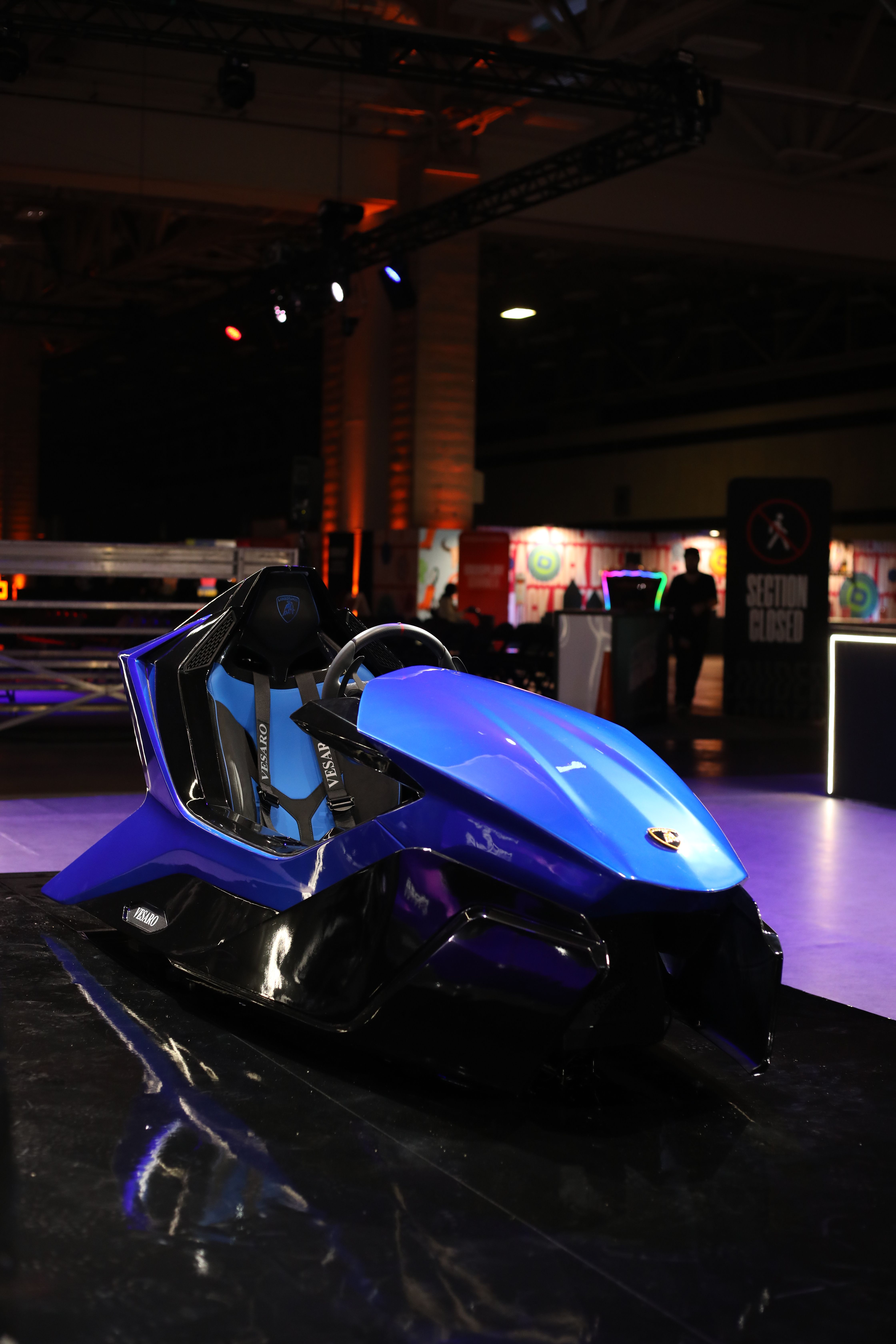 Empty blue Vesaro x Lamborghini simulator on a glossy black plinth in a dark exhibition hall