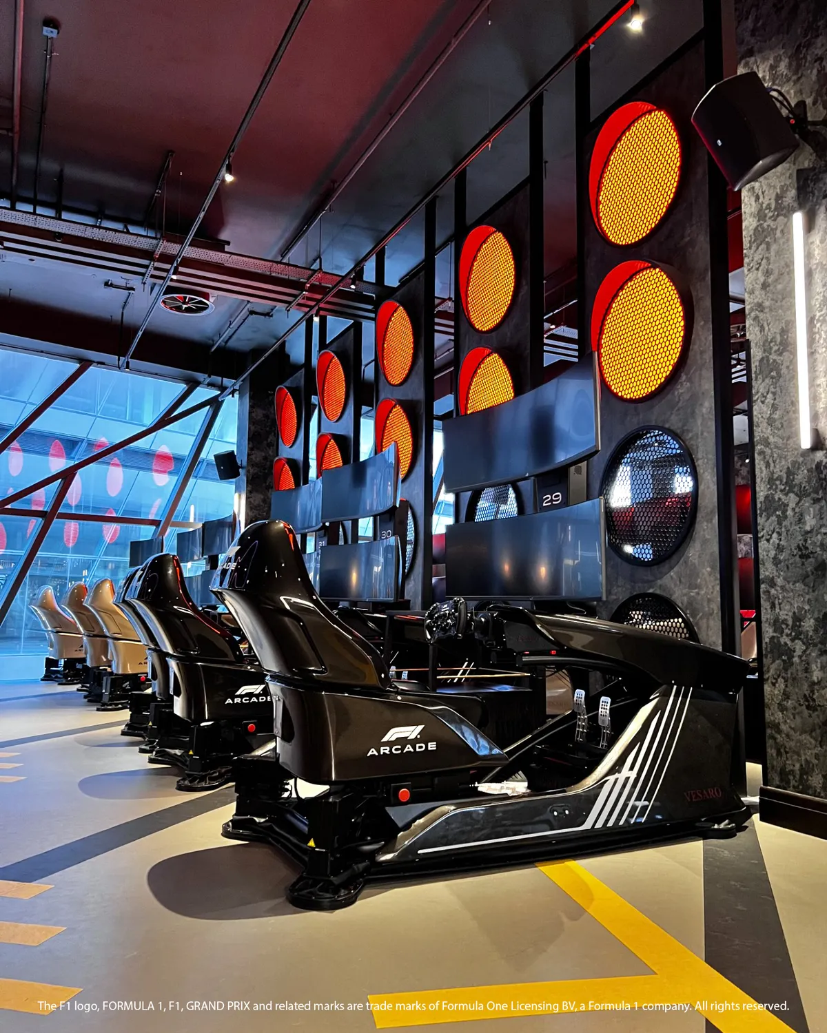 Row of F1 Arcade simulator seats with triple screens in a venue lined with traffic-light style lamps
