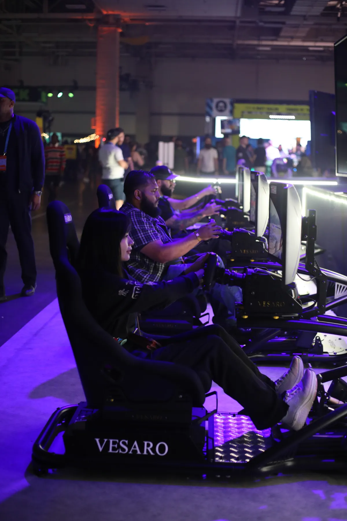 Row of drivers at Vesaro simulators with Vesaro-branded seat bases and monitors in a large event hall