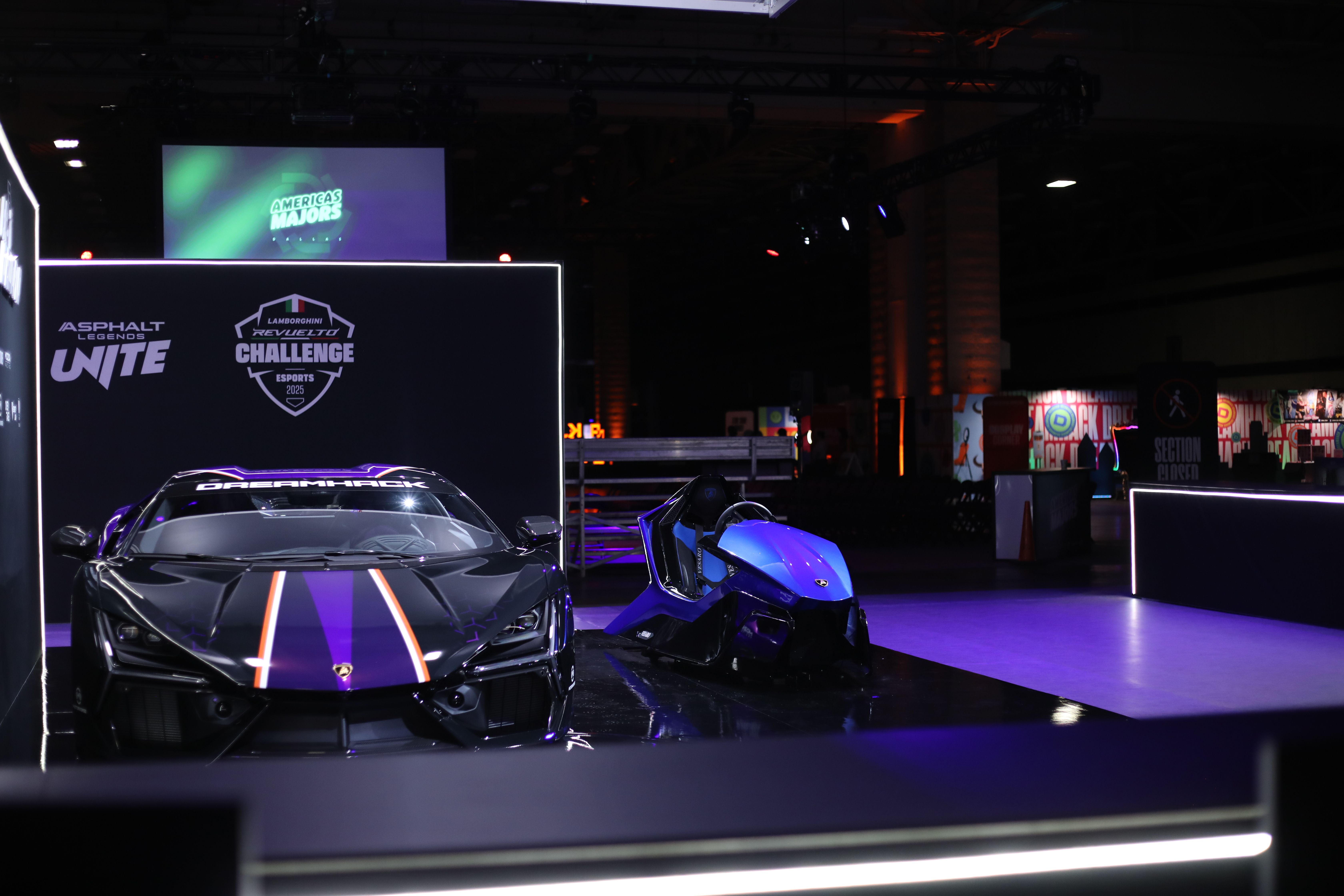 Dark exhibition hall with a black and purple Lamborghini supercar and a blue simulator under purple lighting