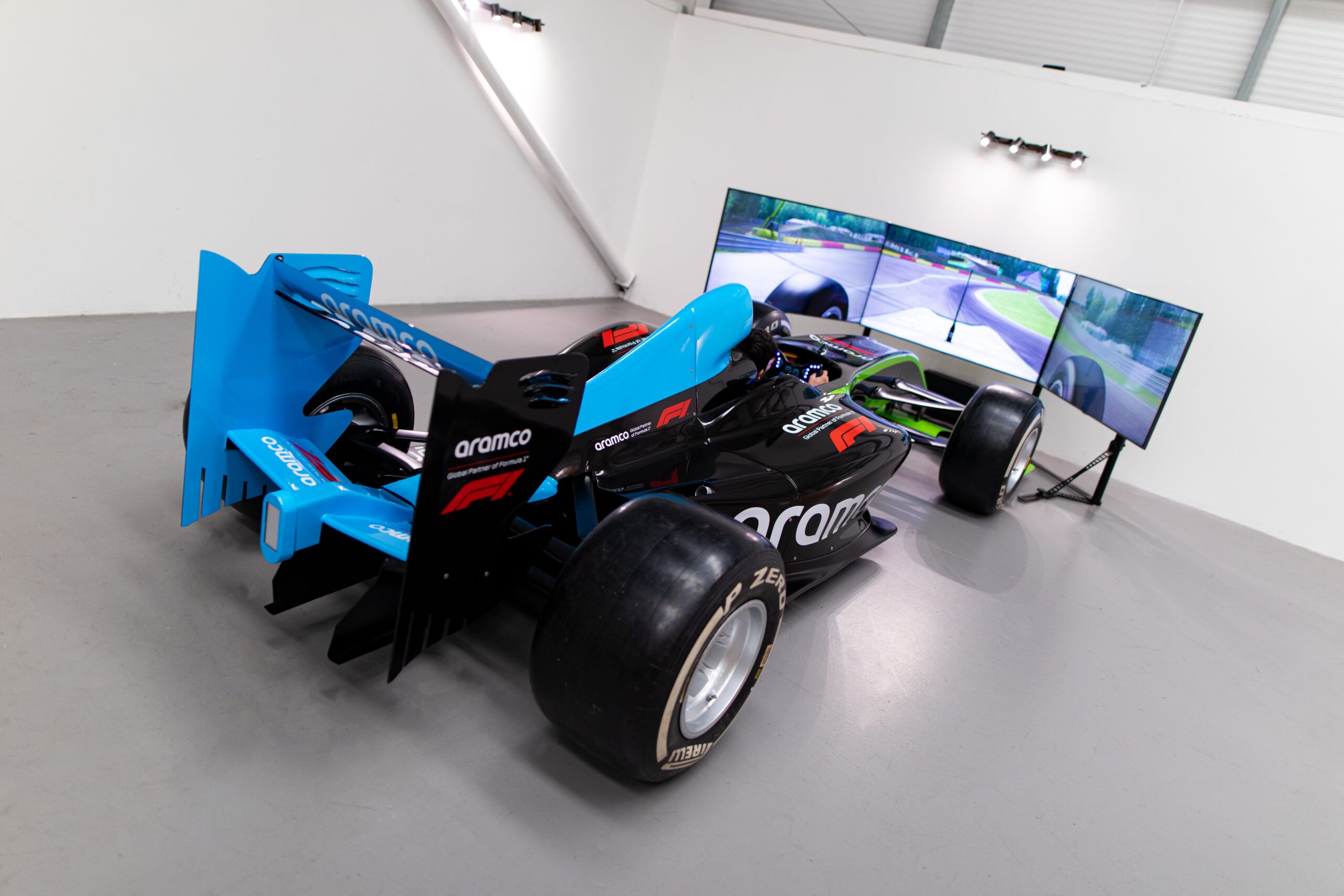 Blue Aramco-liveried F1 style car paired with a triple-screen display in a white showroom