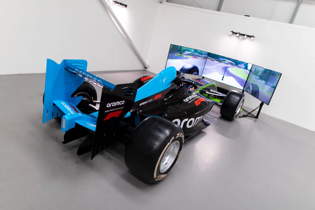 Blue Aramco-liveried F1 style car paired with a triple-screen display in a white showroom