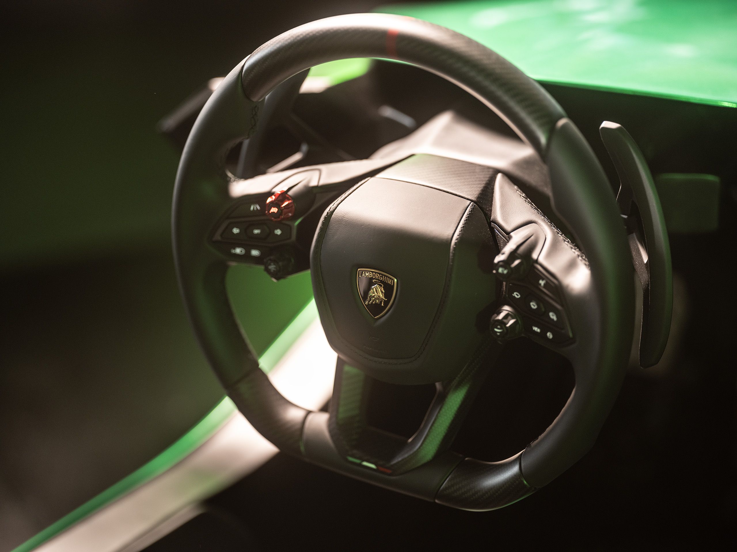 Lamborghini-branded steering wheel with paddle shifters and buttons, green simulator bodywork behind it