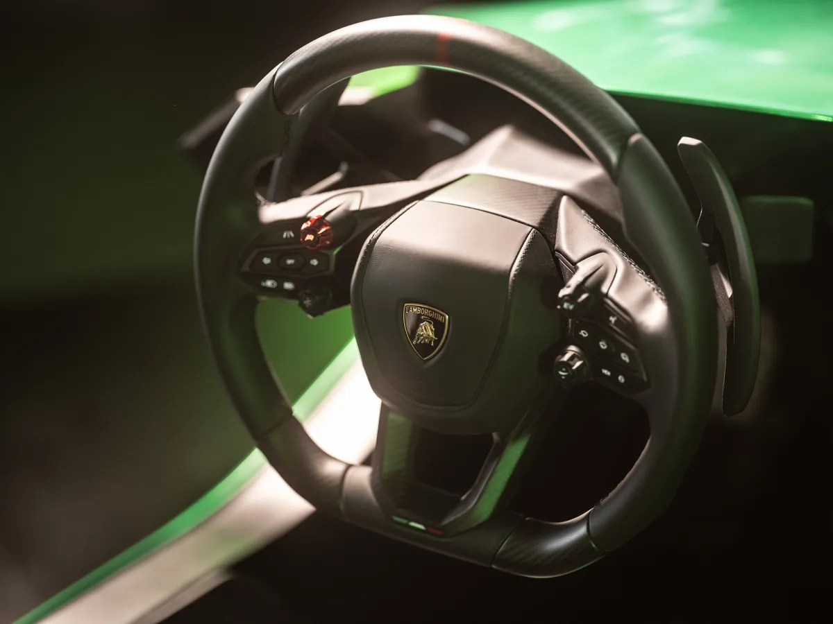 Lamborghini-branded steering wheel with paddle shifters and buttons, green simulator bodywork behind it
