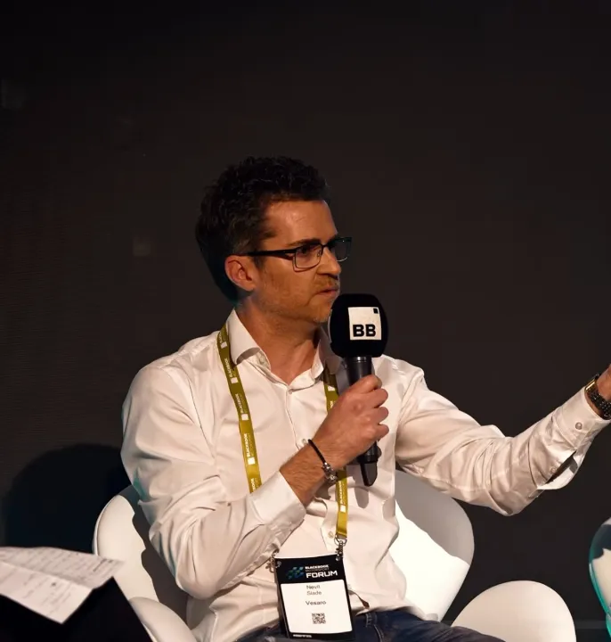 Man with a microphone and a woman with a notebook seated on stage during a panel discussion