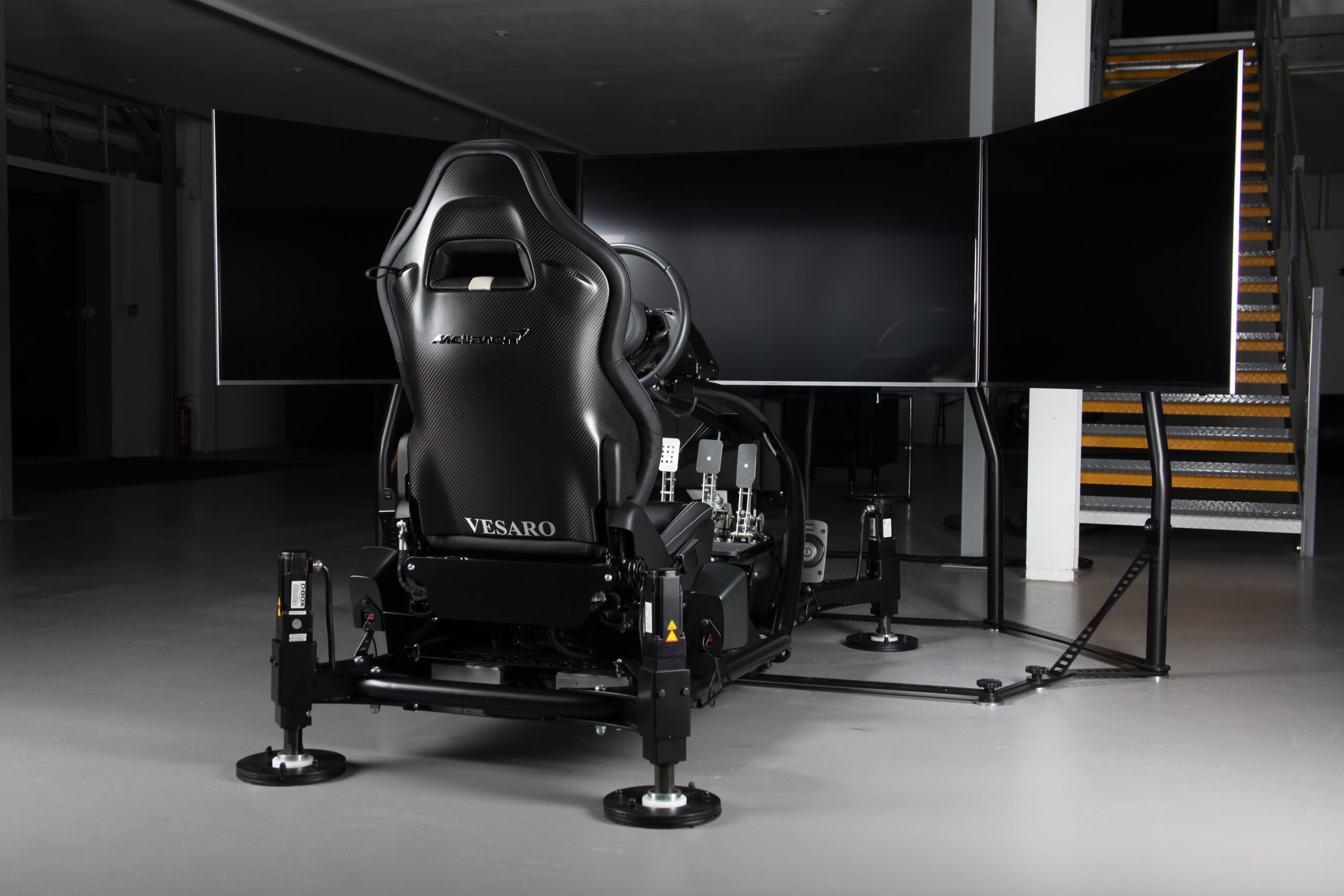 Rear view of a black Vesaro simulator seat on a motion base facing three large screens