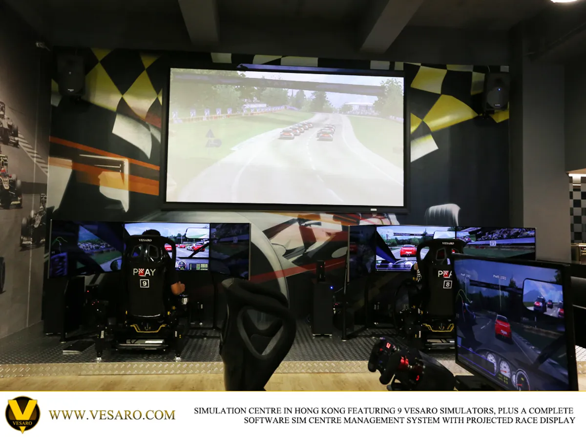 Sim centre with rows of black racing simulators facing a large projected race display and chequered wall graphics