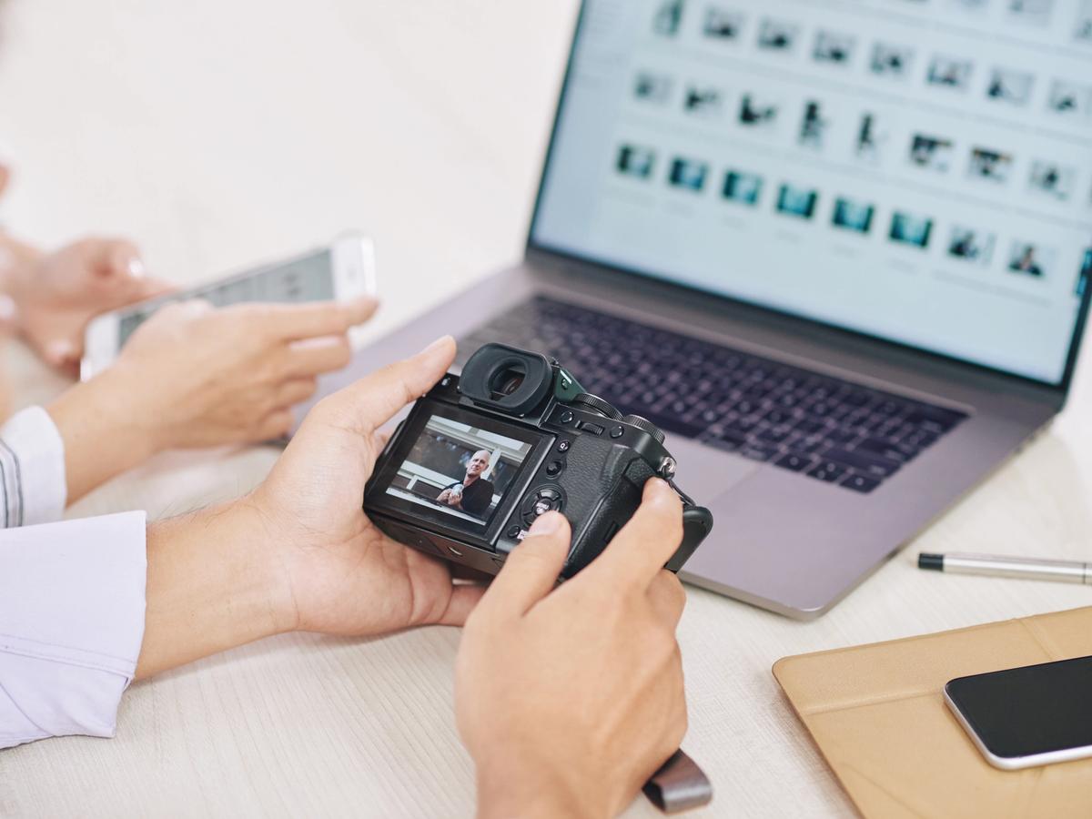 Photographers reviewing images beside a laptop displaying multiple photo thumbnails