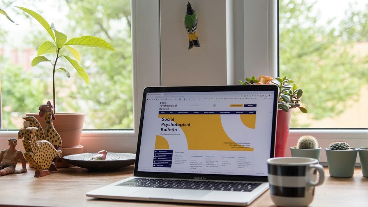 A laptop displaying a website on a wooden desk with potted plants