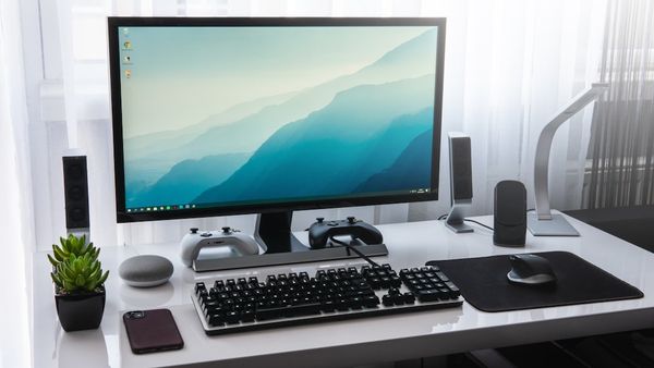 A computer monitor, keyboard, and game controllers on a white desk in a workspace