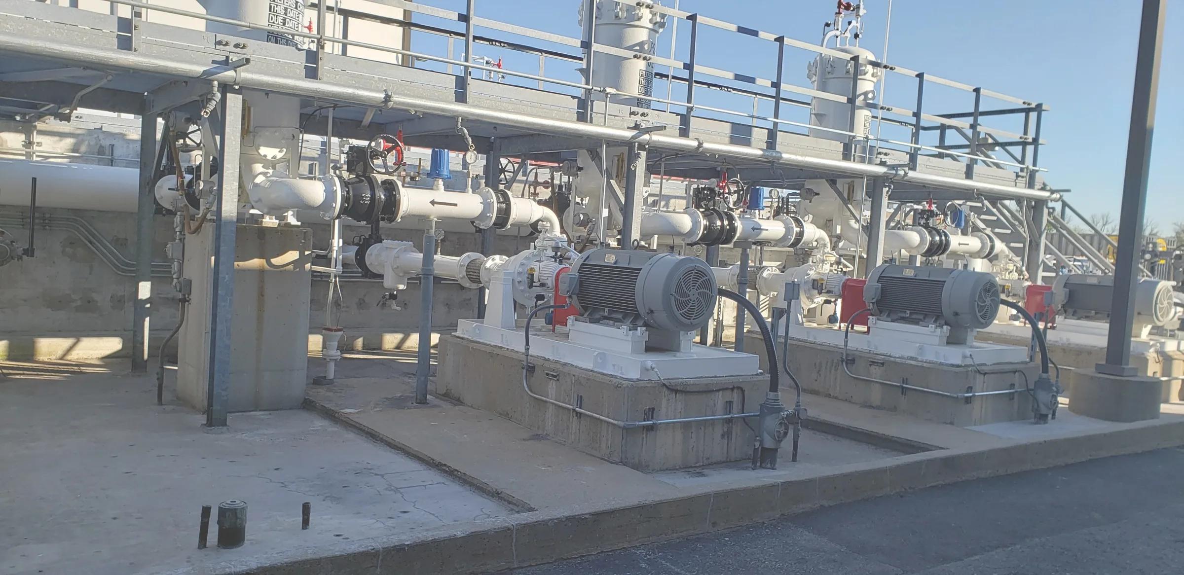Motor-driven pumps on concrete plinths under a pipe rack at an industrial site