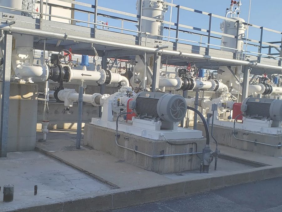 Motor-driven pumps on concrete plinths under a pipe rack at an industrial site