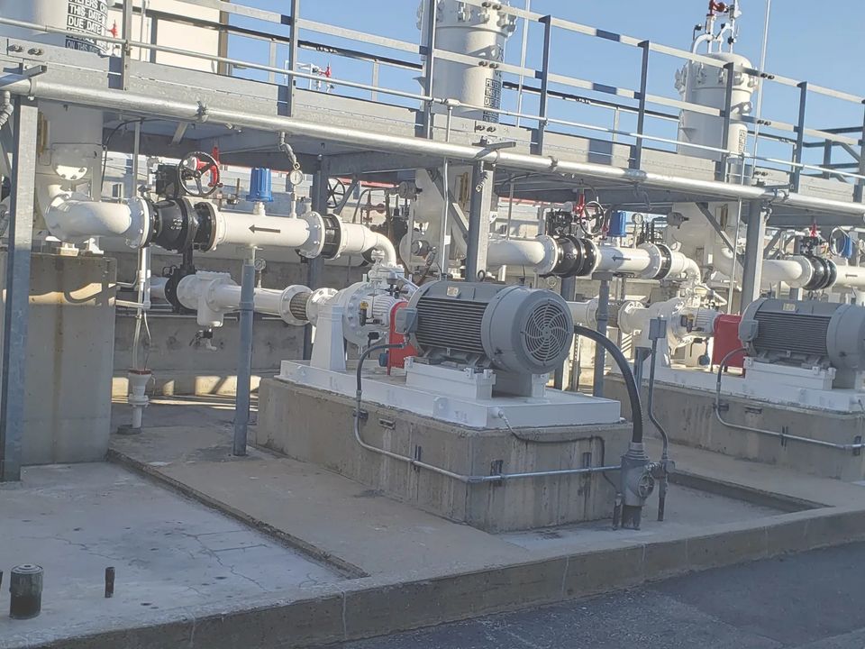 Motor-driven pumps on concrete plinths under a pipe rack at an industrial site