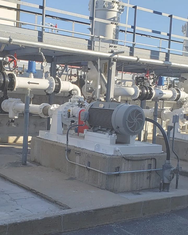 Motor-driven pumps on concrete plinths under a pipe rack at an industrial site