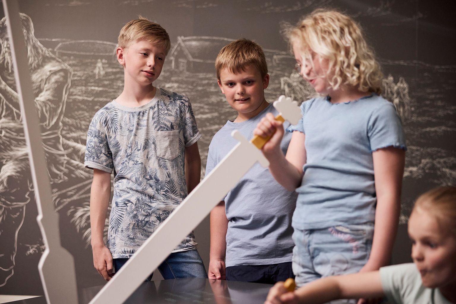 En pige holder et træsværd. To drenge kigger på.