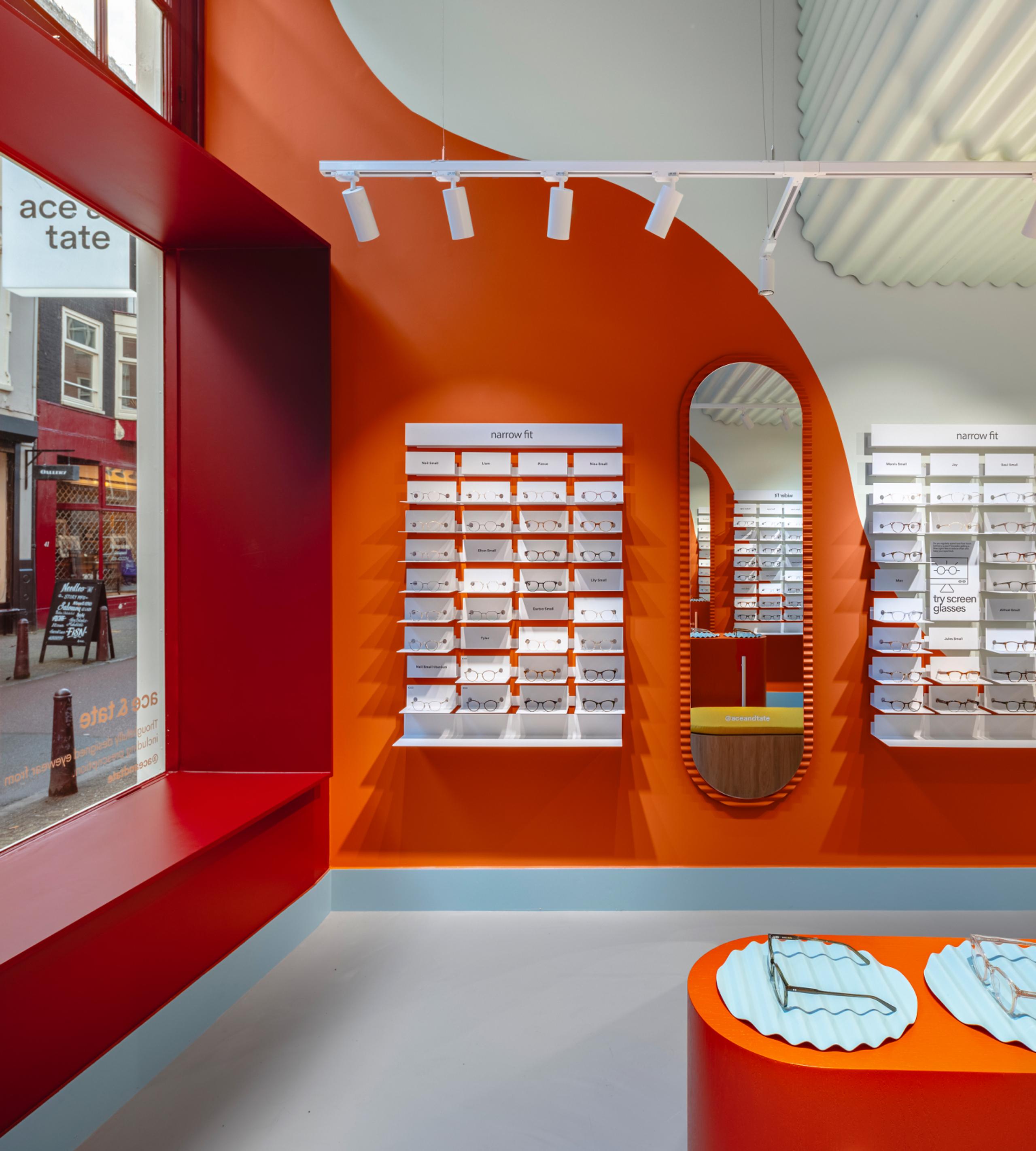 An inviting Ace & Tate Store with bright orange walls and organized shelves displaying a variety of eye glasses for sale.