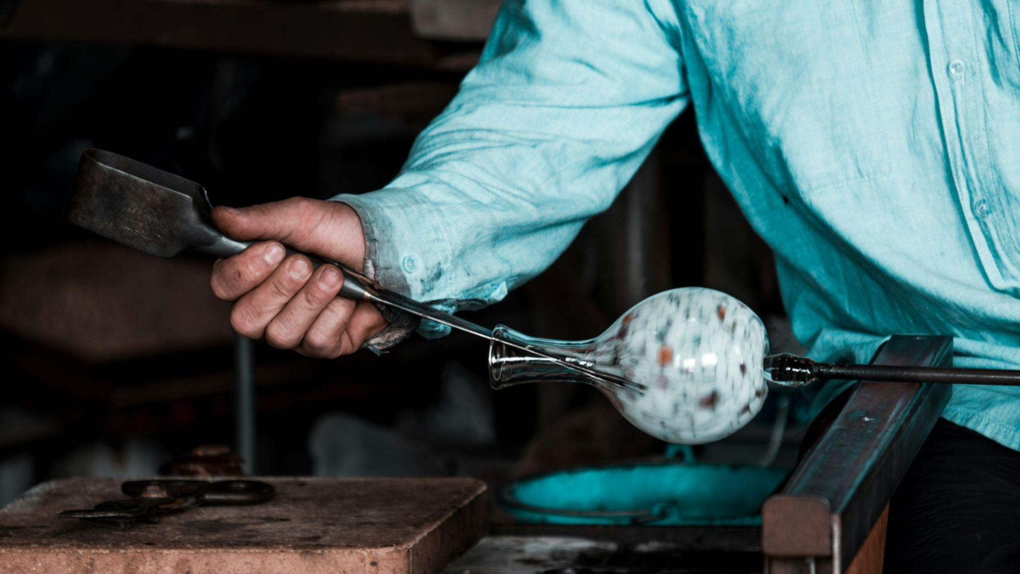 A person uses traditional glass blowing tools to create a vase.