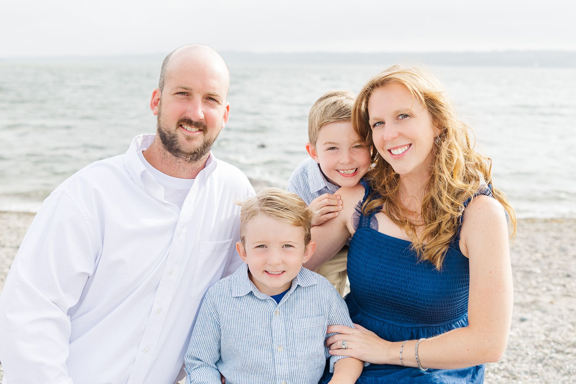 Family of four smiling at the camera on a sandy beach with ocean waves behind them, taken at Seapowet Beach