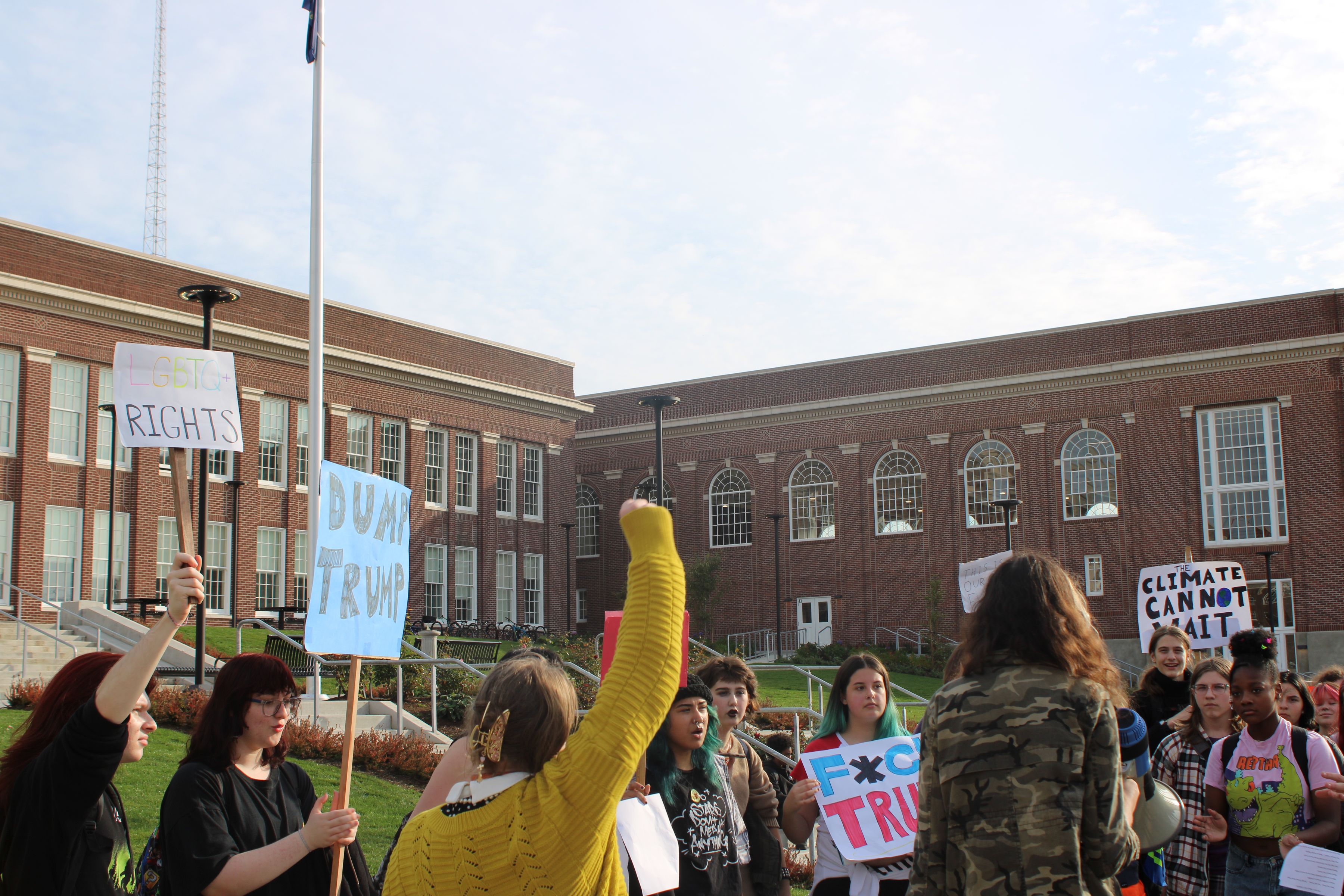 Students protesting in front of Benson Polytechnic High School, with signs that say "LGBTQ+ Rights", "Dump Trump", "Fuck Trump", and "Climate Cannot Wait."