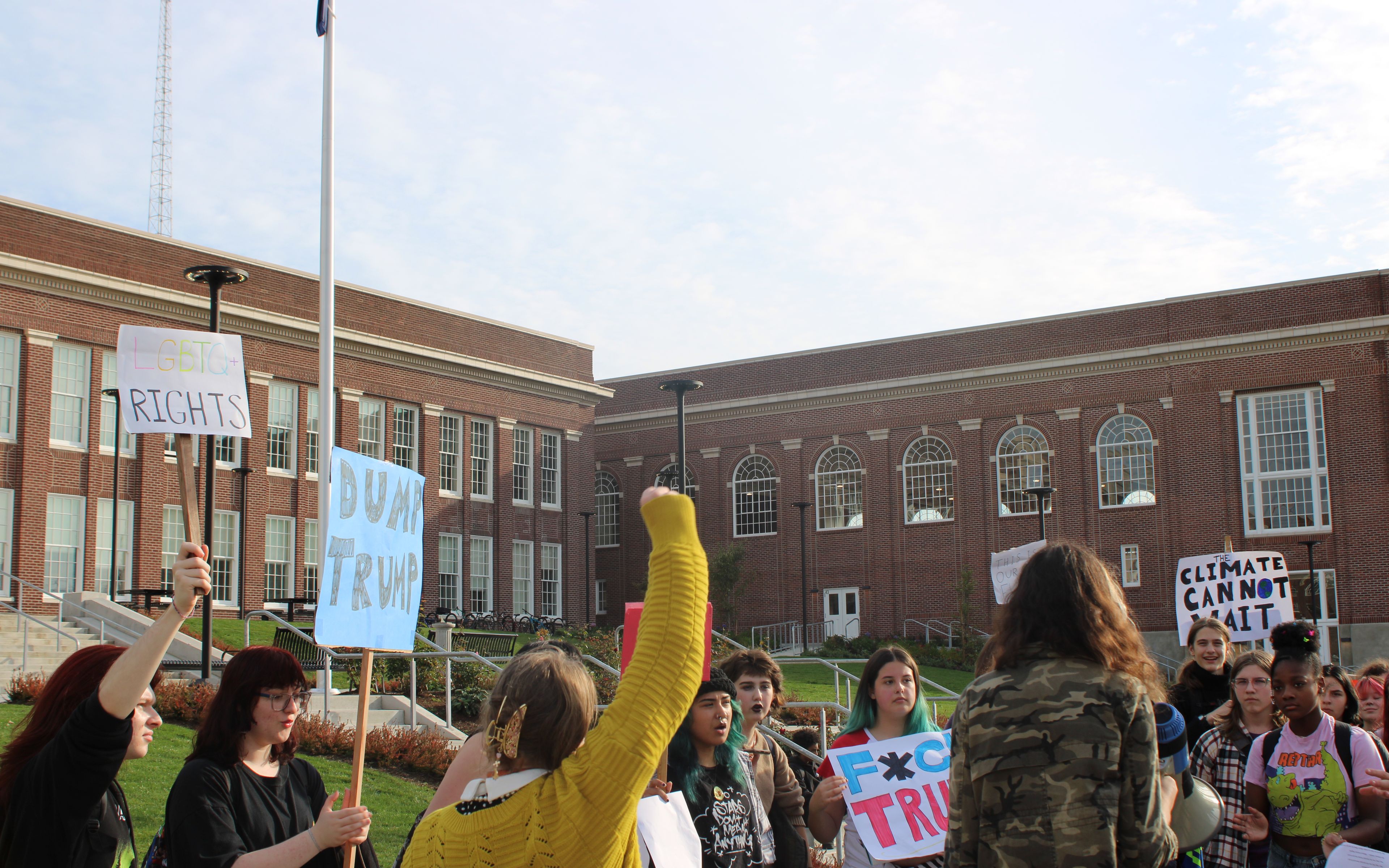 Students protesting in front of Benson Polytechnic High School, with signs that say "LGBTQ+ Rights", "Dump Trump", "Fuck Trump", and "Climate Cannot Wait."