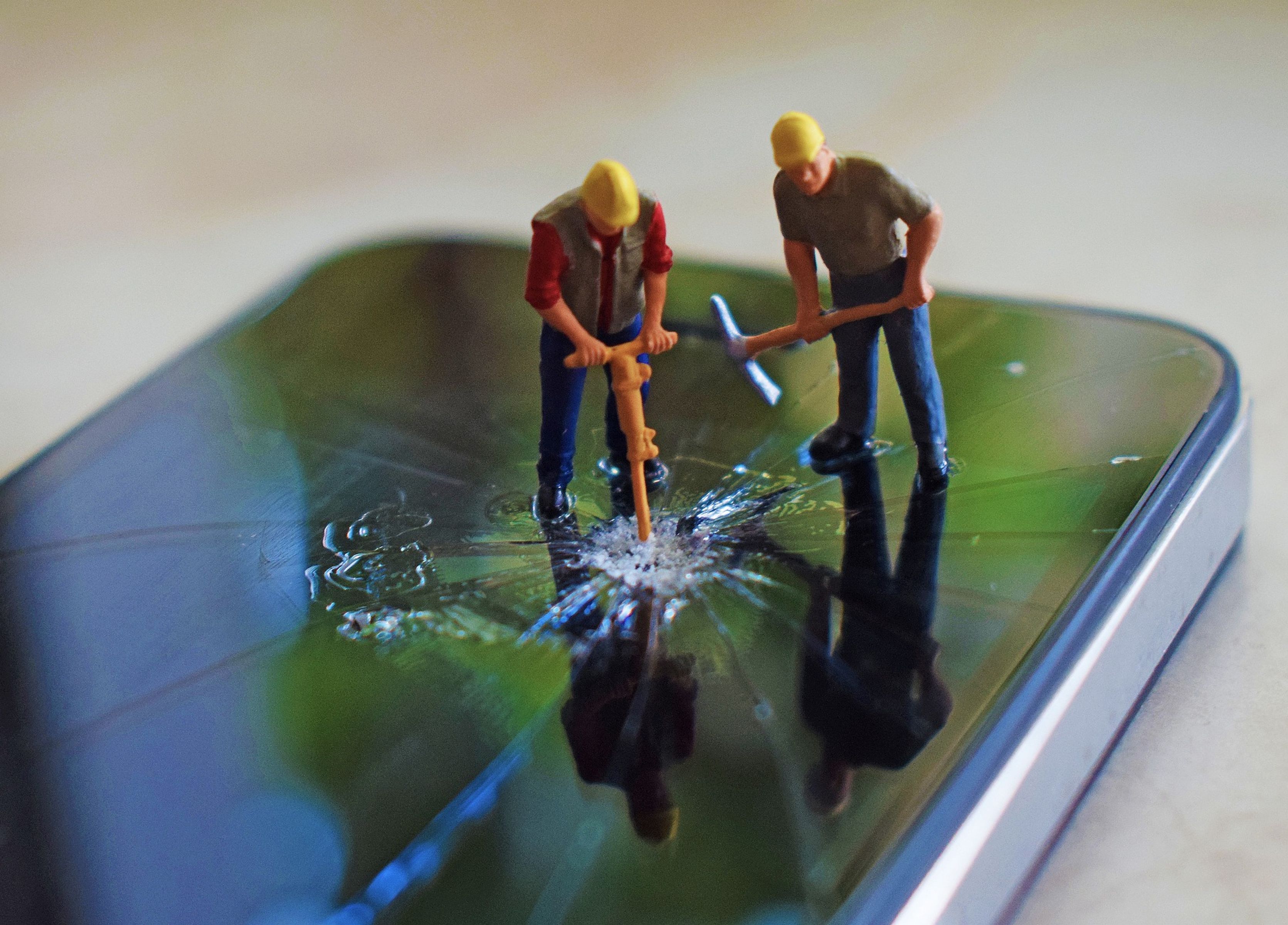 Miniature construction worker figures break a smartphone screen.