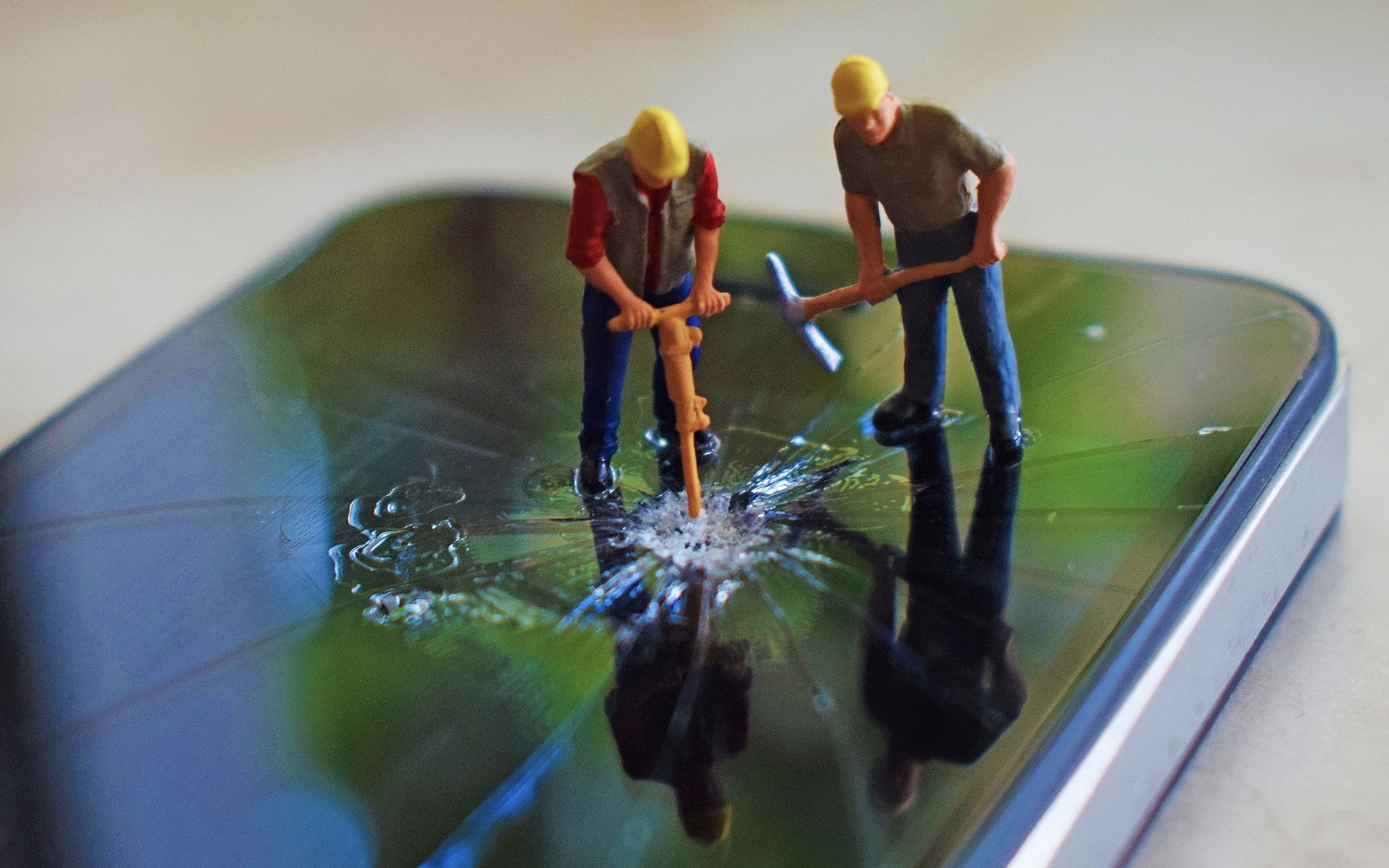 Miniature construction worker figures break a smartphone screen.