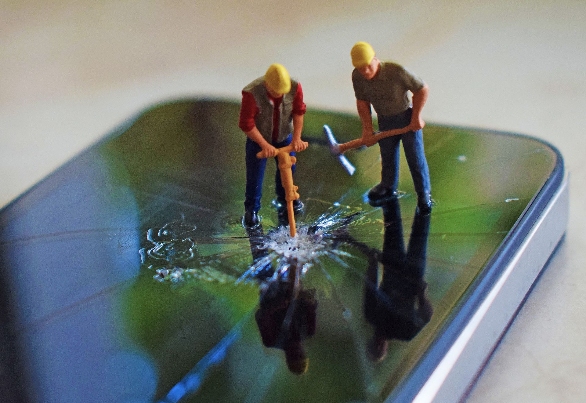 Miniature construction worker figures break a smartphone screen.